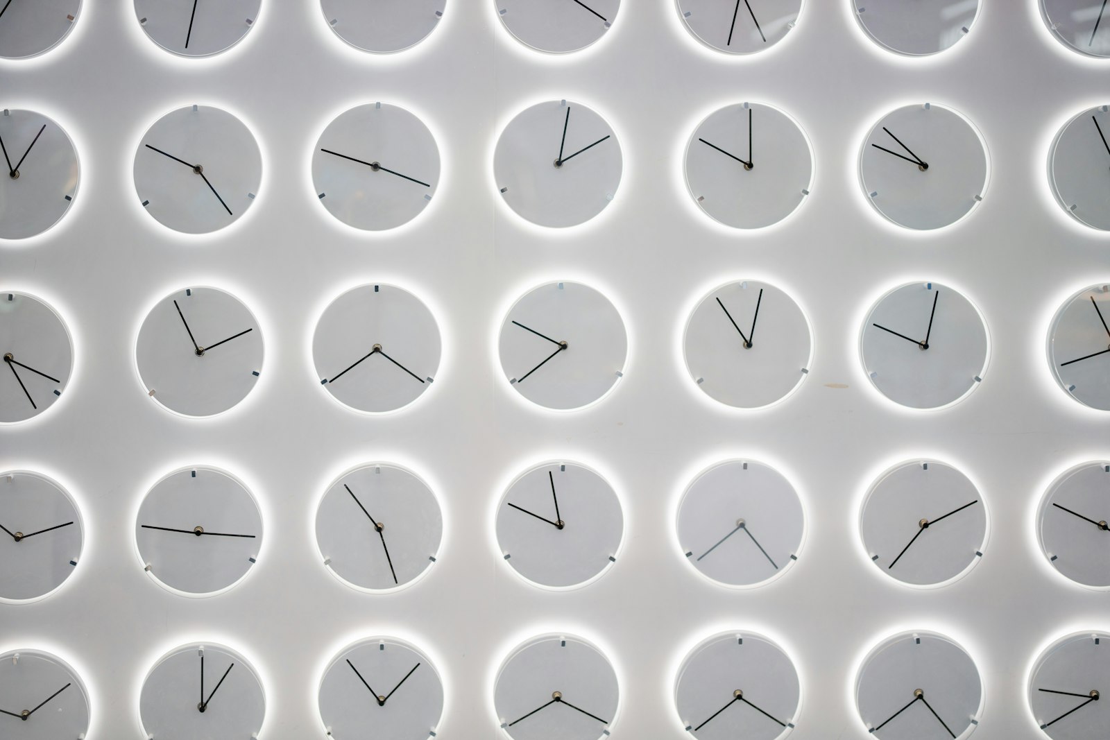 Rows of analog clocks mounted on a wall, each set to a different time zone