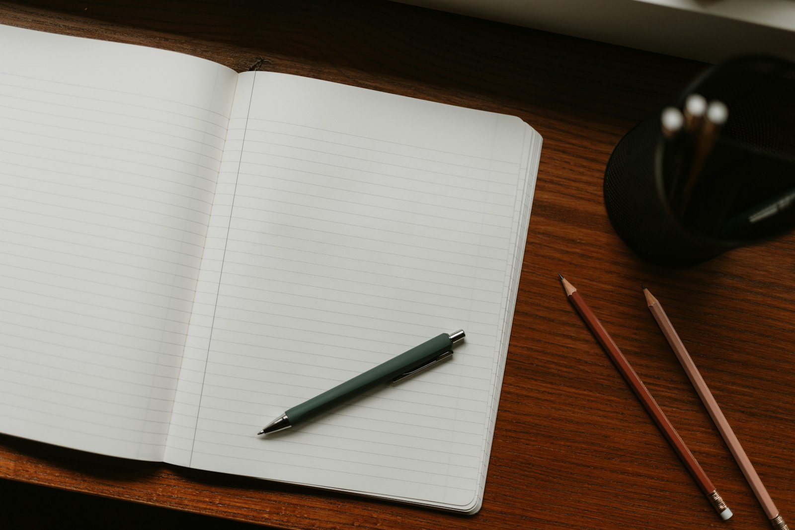 An open notebook with a pen and pencils laid out on a desk for planning