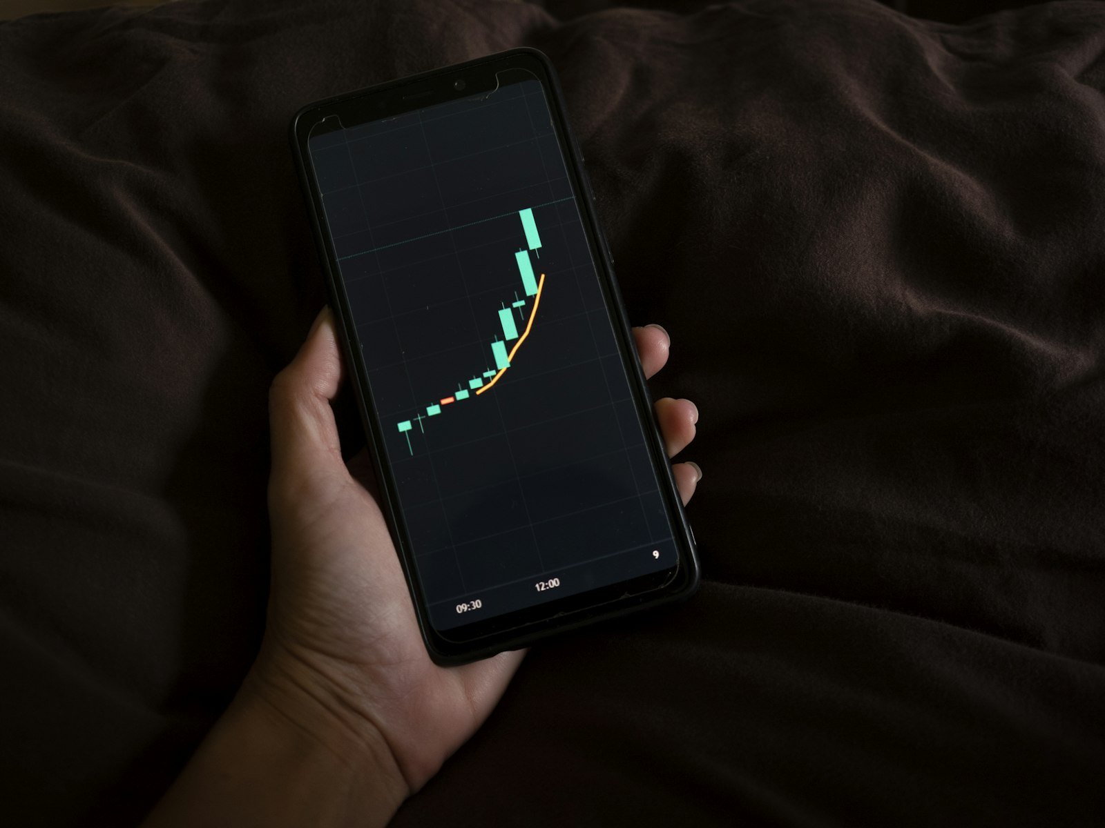 A hand holding a smartphone displaying a trading chart on screen