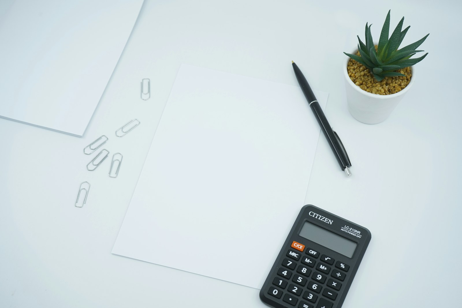 A black calculator and pen resting on blank white paper on a desk